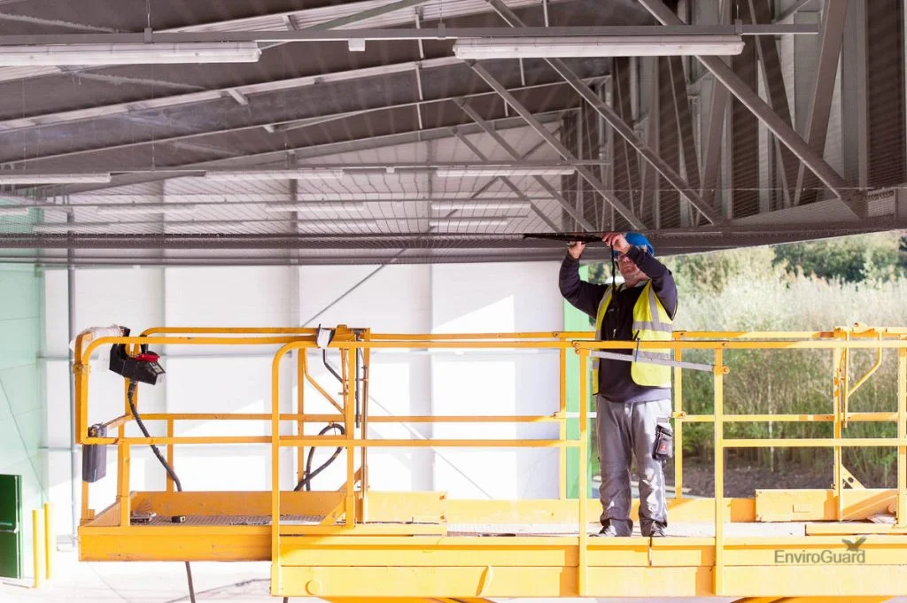 Technician on a scissor lift fixing bird proofing under a steel-framed canopy