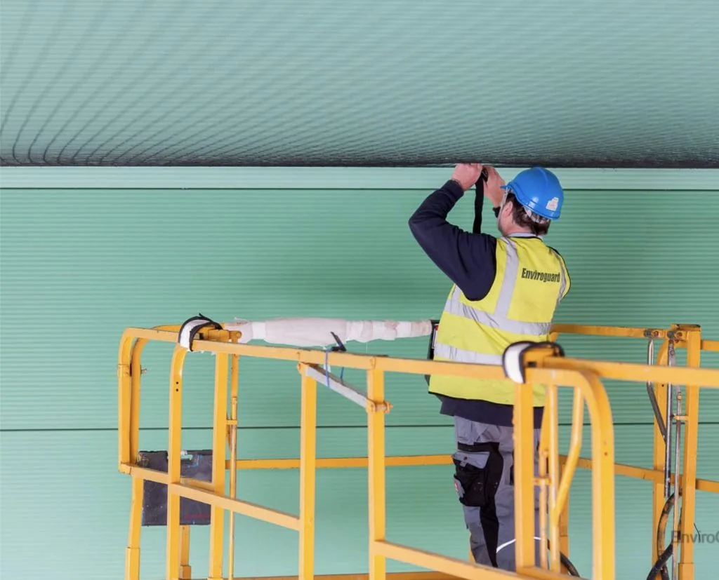 Technician on a scissor lift fitting bird netting beneath a roof canopy